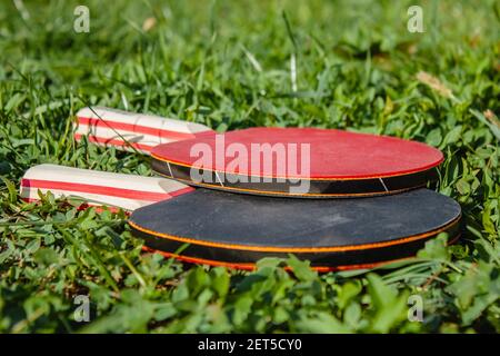 Due racchette da ping pong, rosse e nere, giacciono sull'erba. Primo piano. Il concetto di giochi sportivi all'aperto Foto Stock