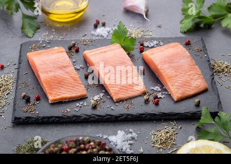 Tre filetti di salmone crudo su ardesia scura su sfondo scuro. Foto Stock