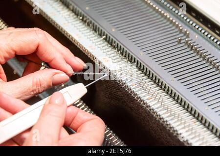 Mani donne che lavorano con la macchina per maglieria, lavorare a maglia come hobby donne. Piccola impresa di produzione di indumenti, moda lenta Foto Stock