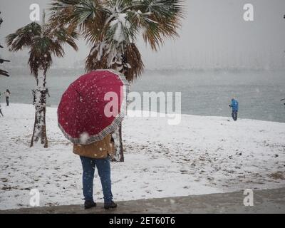 Donna con un ombrello rosso in piedi sulla spiaggia in una tempesta di neve, vicino Atene, Grecia, nel mese di febbraio Foto Stock