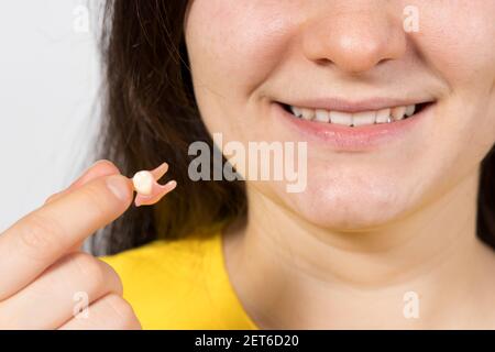 Una paziente femminile di una clinica odontoiatrica tiene in mano un singolo potes - un dente rimovibile in alternativa all'impianto dentale. Foto Stock