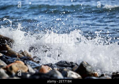 La piccola onda rotola sulla riva e spruzzi di schiuma vola in diverse direzioni. Splendido salvaschermo marino minimalista. Le onde di mare si rompono sul beac di shingle Foto Stock