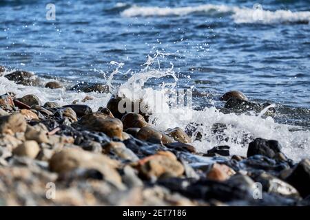 La piccola onda rotola sulla riva e spruzzi di schiuma vola in diverse direzioni. Splendido salvaschermo marino minimalista. Le onde di mare si rompono sul beac di shingle Foto Stock