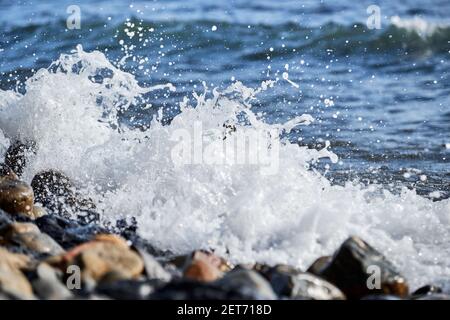 La piccola onda rotola sulla riva e spruzzi di schiuma vola in diverse direzioni. Splendido salvaschermo marino minimalista. Le onde di mare si rompono sul beac di shingle Foto Stock