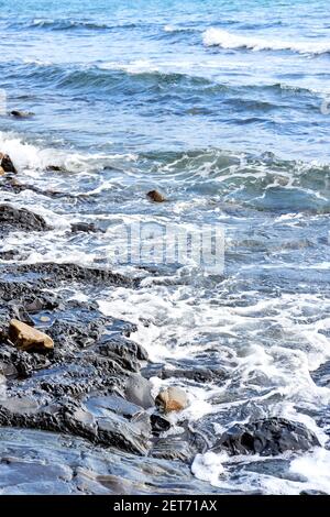 La piccola onda rotola sulla riva e spruzzi di schiuma vola in diverse direzioni. Splendido salvaschermo marino minimalista. Le onde di mare si rompono sul beac di shingle Foto Stock