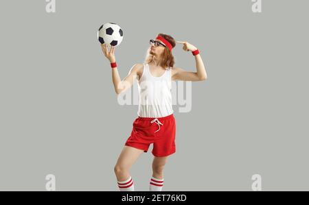 Divertente uomo pazzo nerdy in occhiali, archetto, canotta e pantaloncini che tengono un calcio Foto Stock