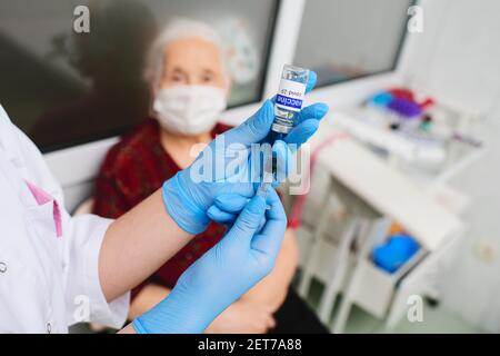 un infermiere contiene una siringa e un vaso di vetro etichettati vaccino covid-19 e si prepara a vaccinare una donna anziana per la prevenzione dell'infettio del coronavirus Foto Stock