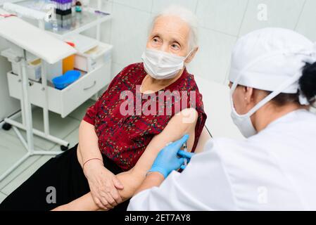 il medico o l'infermiere inietta un farmaco o un vaccino nella spalla di una donna anziana. Foto Stock