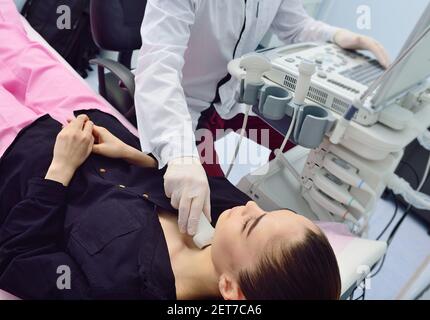 medico in una moderna clinica diagnostica esamina la ghiandola tiroidea di un paziente di una giovane donna attraente su un macchina a ultrasuoni Foto Stock