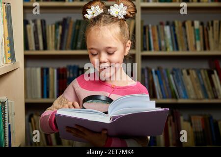 scuola ragazza in piedi con enciclopedia in biblioteca, la lettura di un libro, ottenere nuove informazioni per il cervello Foto Stock