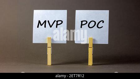 Simbolo MVP vs POC. Stope di legno con fogli bianchi di carta. Parole MVP, prodotto minimo vitale e POC, prova di concetto. Splendido sfondo grigio Foto Stock