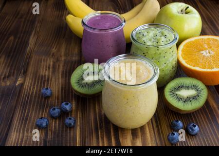 Frullati di frutta diversi o purea in piccoli vasi di vetro su sfondo di legno marrone. Primo piano. Foto Stock