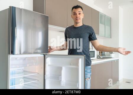 Il ragazzo è triste vicino al frigorifero vuoto senza cibo. Pubblicità del servizio di consegna del cibo. Foto Stock