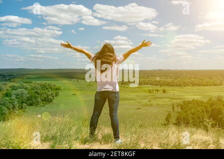 Giovane donna in piedi in un campo di grano con alba sullo sfondo. Una vista dal retro di una donna in piedi su una montagna e ammira la bella Foto Stock