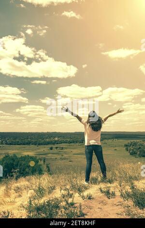 Giovane donna in piedi in un campo di grano con alba sullo sfondo. Una vista dal retro di una donna in piedi su una montagna e ammira la bella Foto Stock