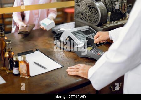 Primo piano immagine ritagliata di donna sconosciuta cliente che acquista farmaci, effettuando il pagamento in farmacia con carta di credito. Uomo farmacista che vortica la carta Foto Stock