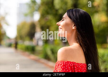 Profilo laterale foto ritratto di allegra donna sorridente indossando elegante abito rosso godendo ventoso clima estivo aria fresca occhi chiusi Foto Stock