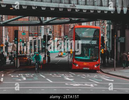 Londra UK Gennaio 2021 Vista di un autobus londinese a due piani che passa sotto un ponte ferroviario. Persone che camminano per le strade durante UK terzo covid nazionale Foto Stock