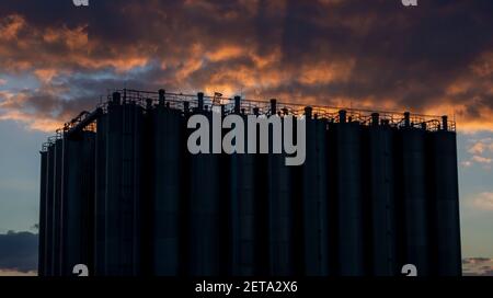 silos industriali in fila, tramonto con cielo drammatico sullo sfondo Foto Stock