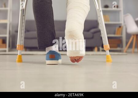 Gambe parte di giovane uomo con gamba rotta in cast camminando con le stampelle a casa Foto Stock