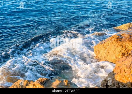 Onde che si infrangono sulle rocce sulla spiaggia al mattino. Alba sul mare ondulato con rocce Foto Stock