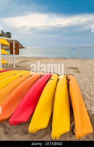 un centro di noleggio di kayak, canoe e attrezzature nautiche, con kayak gialli, arancioni e rossi sulla sabbia di una spiaggia con acque cristalline Foto Stock