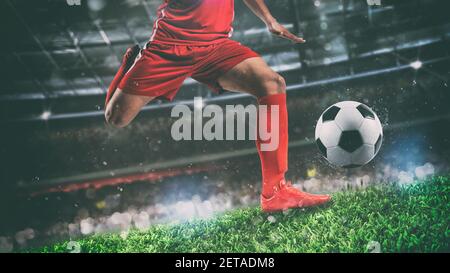 Primo piano di una scena di calcio durante la partita notturna con giocatore in una divisa rossa calcia la palla con il potere Foto Stock