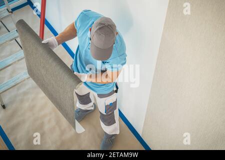 Ristrutturazione degli interni. Lavoratore caucasico nei suoi 40 anni di preparazione di carta da parati in vinile per Wall applicare. Tema industriale. Foto Stock