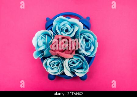 Fiori di rosa blu e rosa in un orologio blu su sfondo rosa. Disposizione piatta Foto Stock