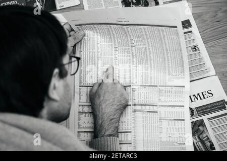 Parigi, Francia - Feb 13, 2021: POV mano maschile lettura FT week-end Financial Times guardando con attenzione sui dati di mercato di diverse società pubbliche grafici - spettacoli in possesso Foto Stock