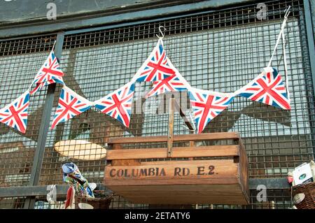 Union Jack o Bandiera che si accatastano sopra la scatola del trug con Columbia Road, E2 stampato sul lato del negozio esterno nel mercato Foto Stock