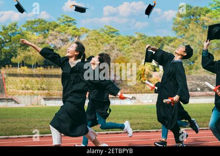 Felici gli studenti con le congratulazioni che gettano i cappelli di laurea in aria per festeggiare Foto Stock