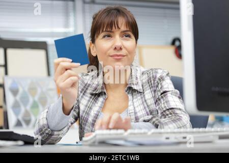 donna moderna che usa il computer alla scrivania mentre controlla il campione Foto Stock