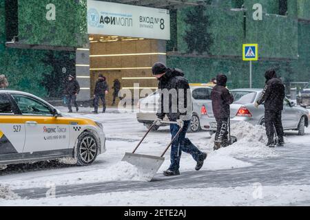 Mosca. Russia. 12 febbraio 2021. Un addetto alla pubblica utilità rimuove la neve con uno scraper su una strada cittadina durante una nevicata in una giornata invernale. labo fisico duro Foto Stock