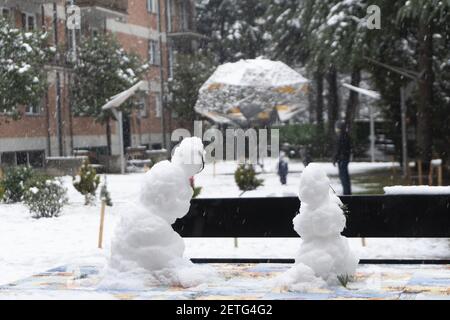 Papà e figlio giocano nel parco giochi durante una nevicata. Un paio di pupazzi di neve in primo piano. Grandi fiocchi di neve. Divertimento invernale Foto Stock