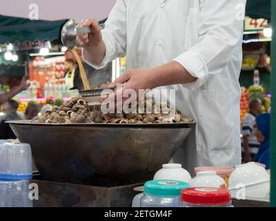 cuoco che serve escargot in un ristorante all'aperto nel mercato jemaa el-fnaa di marrakech, morro Foto Stock