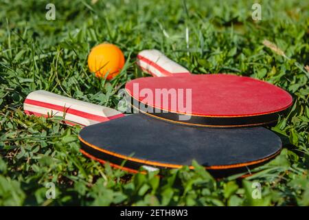 Due racchette da ping pong e una palla arancione giacciono sull'erba. Il concetto di giochi sportivi all'aperto Foto Stock