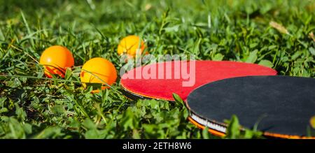 Due racchette da ping pong e tre palline arancioni giacciono nell'erba. Il concetto di giochi sportivi all'aperto Foto Stock