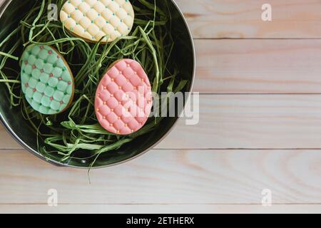 Colorati pasqua biscotti fatti a mano uova nel nido su sfondo di legno chiaro. Disposizione piatta, vista dall'alto Foto Stock