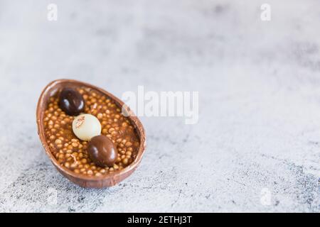 Mezzo uovo di cioccolato riempito con riso schioccato e piccole uova di shocolade. Spazio di copia Foto Stock