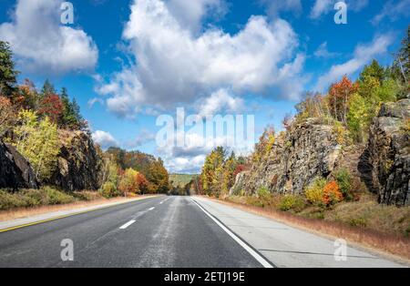 Affascinante e colorata e tortuosa strada statale del New Hampshire fiancheggiata da autunno aceri alberi su rocce e scogliere invita il viaggiatore su un viaggio indimenticabile Foto Stock