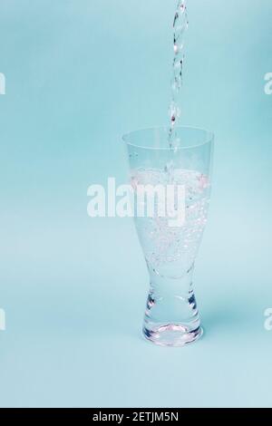 Un getto d'acqua riempie il vetro trasparente su uno sfondo blu. Le bolle bianche aumentano. Foto Stock