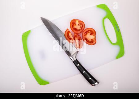 Su un tagliere c'è un pomodoro fresco tagliato rosso e un grande coltello da chef. Su uno sfondo bianco isolato. Foto Stock