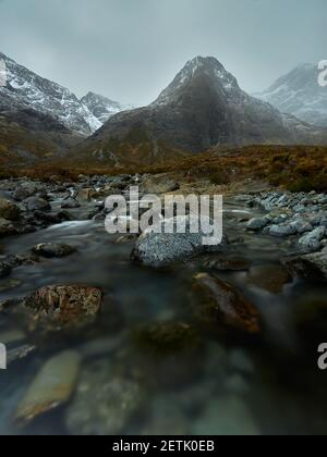 acqua trasparente con rocce e grande picco sullo sfondo Con neve in inverno - piscine fairy - Skye Island - Scozia - Regno Unito Foto Stock