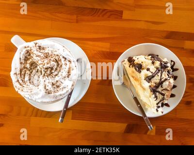 Cappuccino. Una tazza di cappuccino, latte si trova su un tavolo di legno con una fetta dolce di cake conte rovine Foto Stock