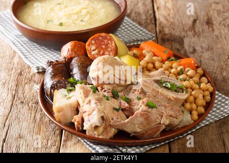 Il cocido è un tradizionale stufato a base di ceci con pollo, manzo, salsiccia di sangue, chorizo e pancia di maiale da vicino su un piatto sul tavolo. Orizzontale Foto Stock