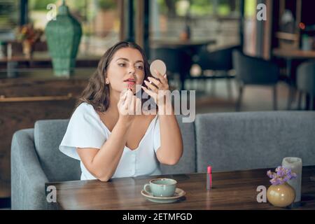 Donna che dipinge le labbra con rossetto nel caffè Foto Stock