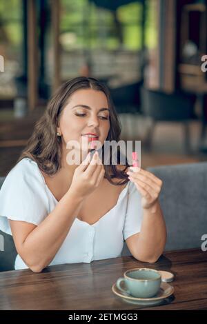 Donna che dipinge le labbra seduti nel caffè estivo Foto Stock