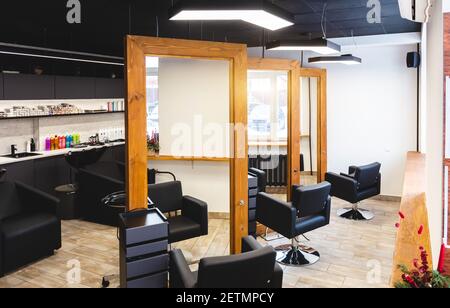 Salone di bellezza interno barbiere. Grandi specchi incorniciati in legno e comode poltrone in pelle nera in uno spazio moderno, accogliente e luminoso. Foto Stock