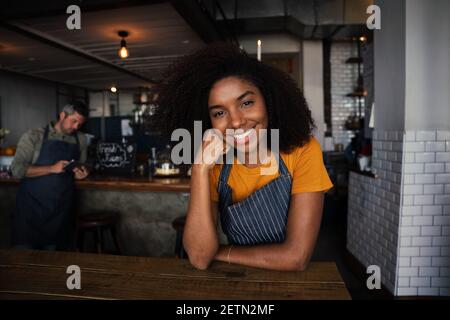 Bella femmina etnica sorridente appoggiata al gomito in un caffè funky negozio Foto Stock